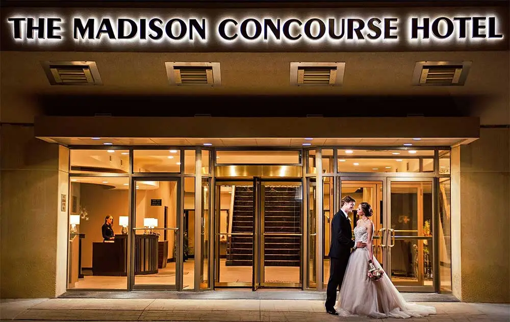 A couple is standing outside of the madison concourse hotel.