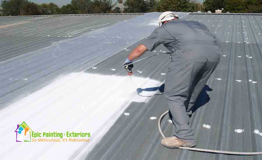 A man spraying white paint on the roof of a building.