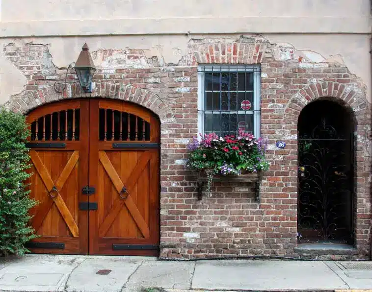 A brick building with two wooden doors and flowers in the window.